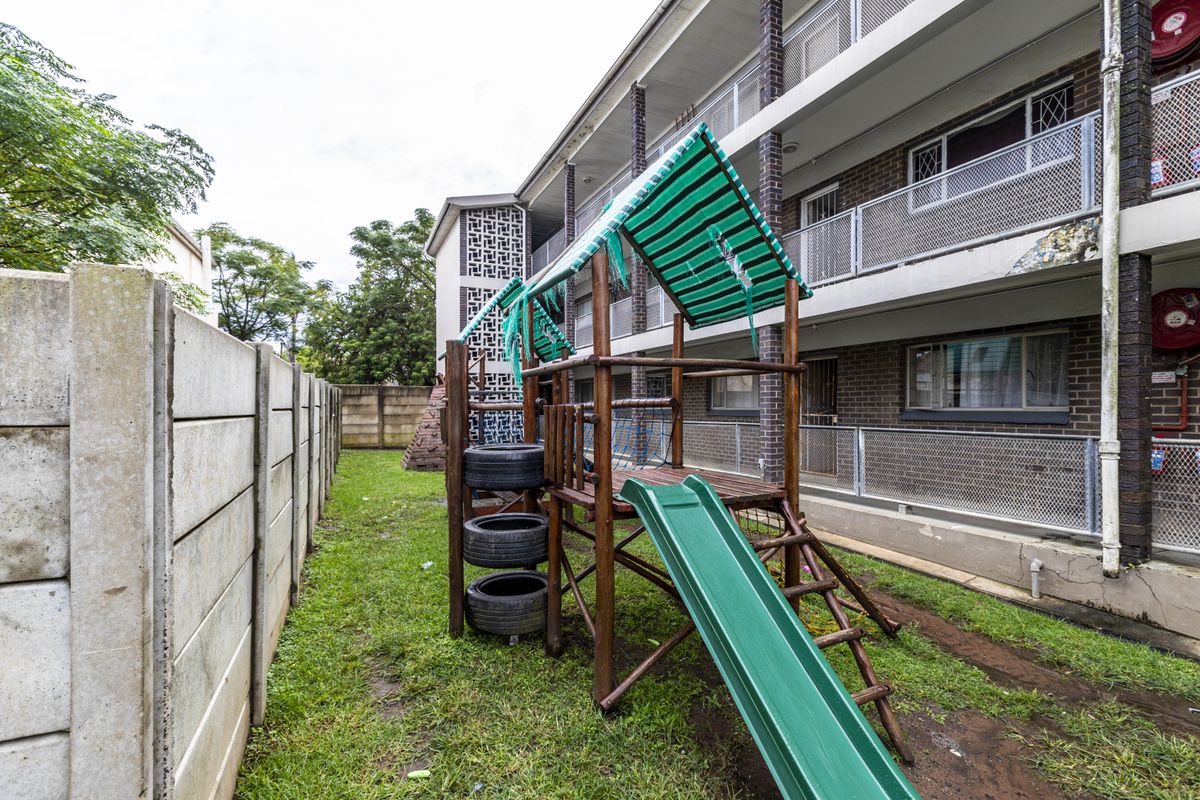 Rear exterior view of the apartment building featuring a communal garden area with a precast concrete boundary wall and metal security balustrades.