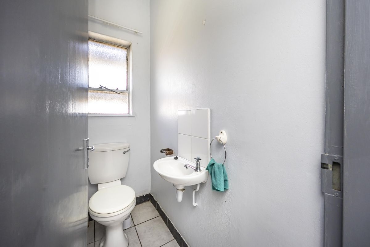 A compact bathroom featuring a standard toilet, wall-mounted basin, and tiled flooring, requiring cosmetic updates to improve its overall condition.
