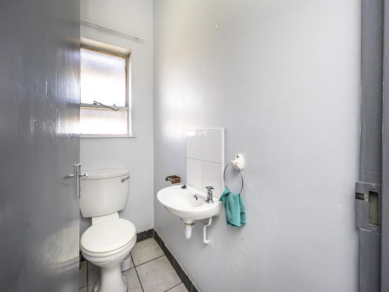 A compact bathroom featuring a standard toilet, wall-mounted basin, and tiled flooring, requiring cosmetic updates to improve its overall condition.