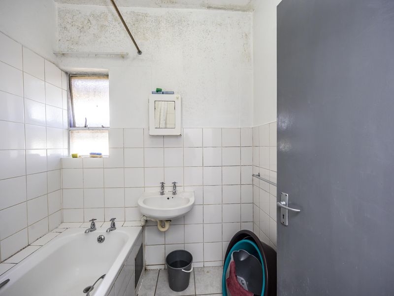 A dated bathroom featuring a standard bathtub, wall-mounted basin, and tiled finishes, currently requiring maintenance and cosmetic updates to the ceiling and wall surfaces.