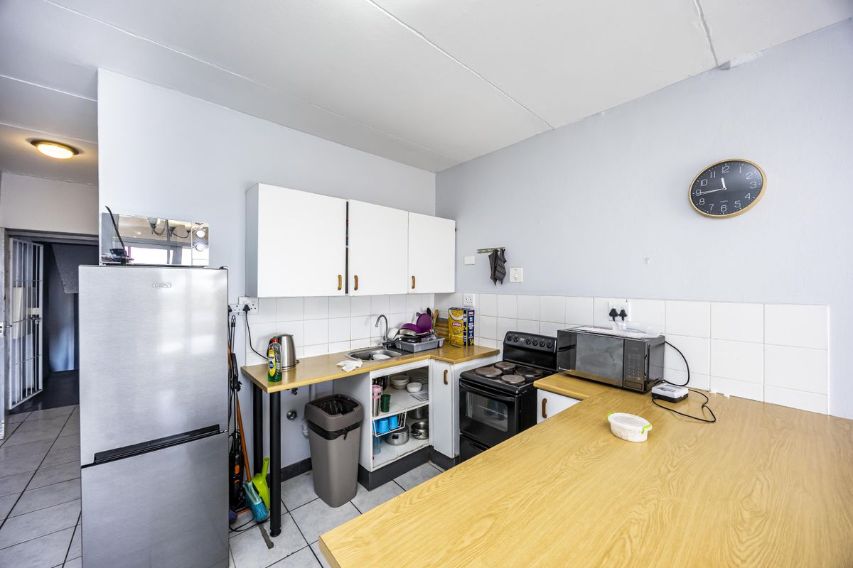 Compact kitchen featuring white cabinetry, tiled backsplash, laminate countertops, and a freestanding stove, with an open-plan layout and tiled flooring.