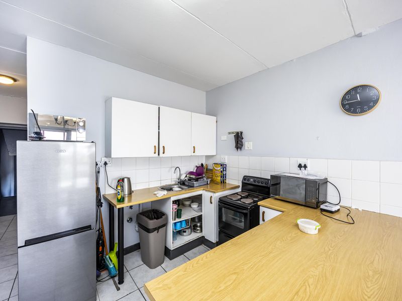 Compact kitchen featuring white cabinetry, tiled backsplash, laminate countertops, and a freestanding stove, with an open-plan layout and tiled flooring.