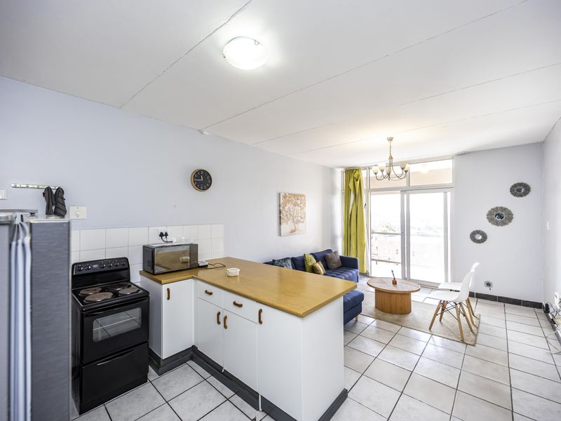 Open-plan living area featuring a functional kitchen with a freestanding stove, tiled flooring, and direct access to a balcony through sliding glass doors.