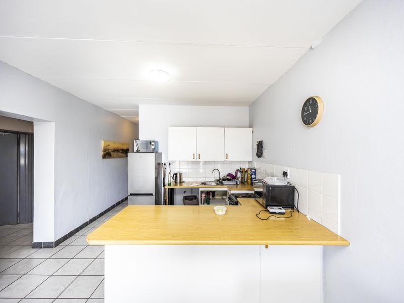 A functional kitchen area featuring white cabinetry, a laminate breakfast bar, tiled backsplash, and ceramic floor tiles.