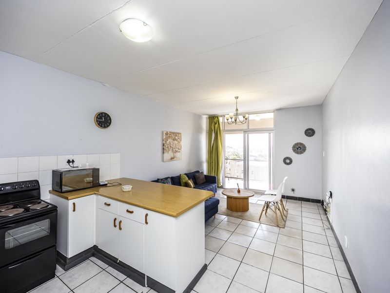 Open-plan living area featuring a functional kitchen with tiled flooring, built-in cabinetry, and direct access to a balcony through sliding glass doors.