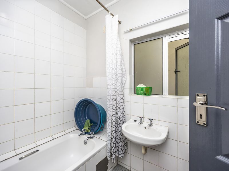 A compact bathroom featuring a bathtub, wall-mounted basin, and white tiled walls, requiring some maintenance and cosmetic updates.