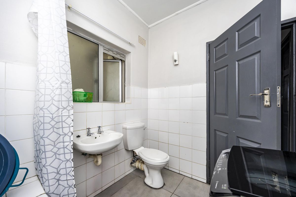 A functional bathroom featuring a wall-mounted basin, toilet, and tiled finishes, requiring some maintenance and cosmetic updates to improve its overall condition.