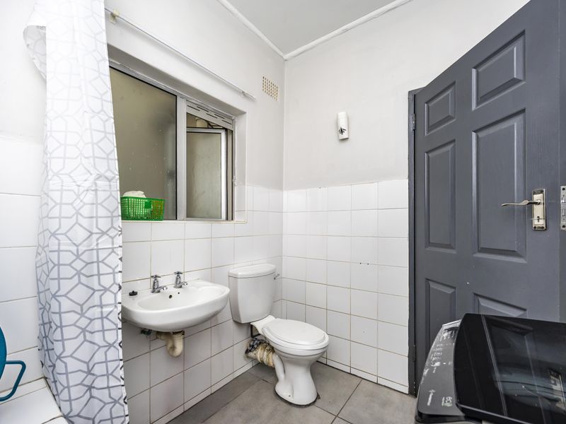 A functional bathroom featuring a wall-mounted basin, toilet, and tiled finishes, requiring some maintenance and cosmetic updates to improve its overall condition.