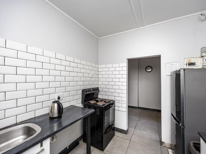 A compact kitchen featuring a subway tile backsplash, dark laminate countertops, a stainless steel sink, and a freestanding electric stove.