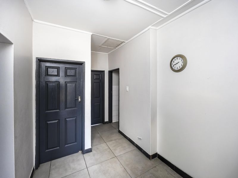 A functional hallway featuring neutral tiled flooring and dark-painted panelled doors, providing access to various rooms within the apartment.