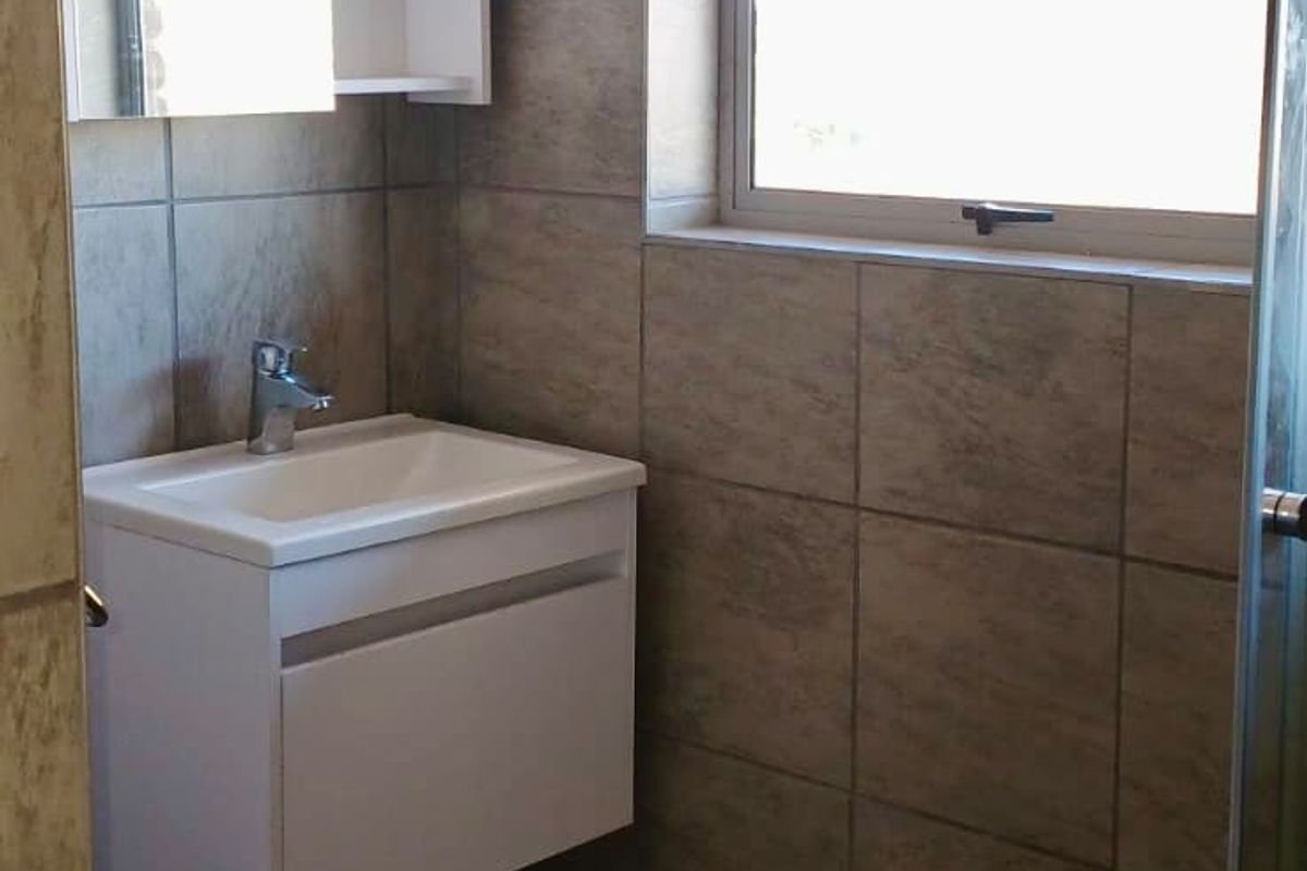 A compact bathroom featuring a wall-mounted vanity, tiled finishes, and a shower enclosure, currently requiring minor finishing work to the ceiling area.