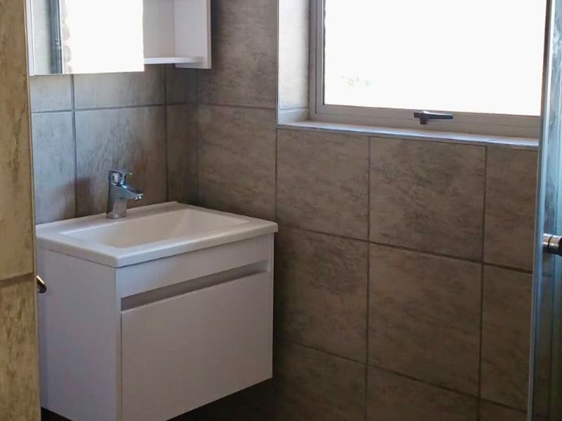 A compact bathroom featuring a wall-mounted vanity, tiled finishes, and a shower enclosure, currently requiring minor finishing work to the ceiling area.