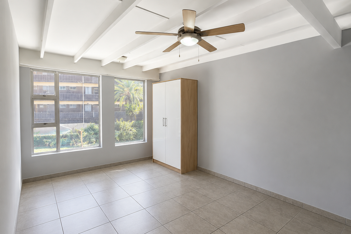 A bright, spacious bedroom featuring exposed ceiling beams, a ceiling fan, neutral tiled flooring, and a built-in wardrobe.