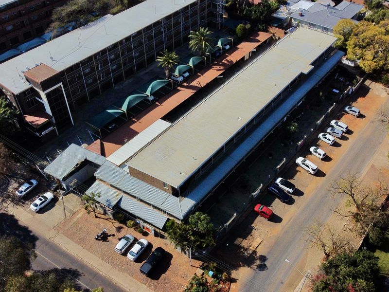 Aerial view of the apartment complex featuring a long building structure, covered parking bays, and paved driveway access.
