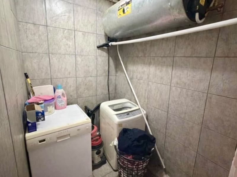 A functional laundry area featuring fully tiled walls and floor, equipped with essential plumbing connections and a wall-mounted electric water heater.