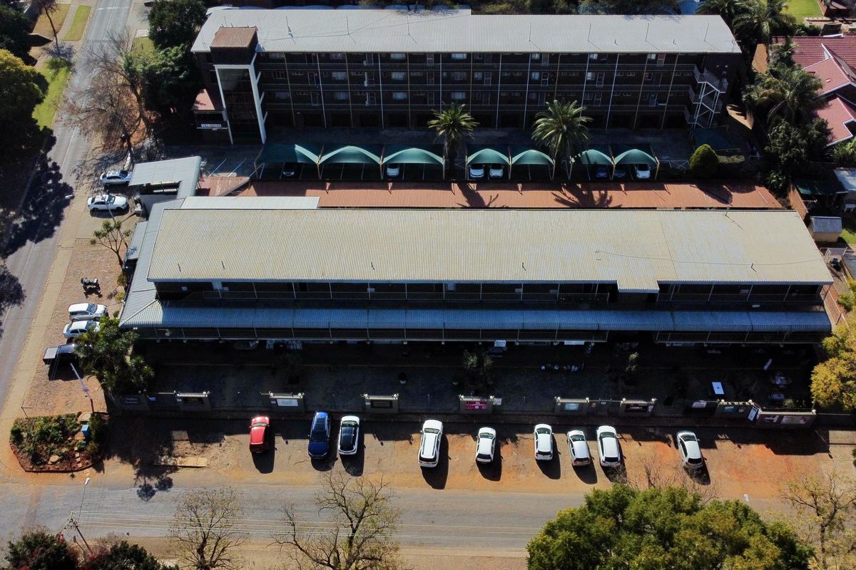 Aerial view of a multi-story apartment complex featuring a corrugated metal roof, dedicated shade cloth carports, and an adjacent paved parking area.
