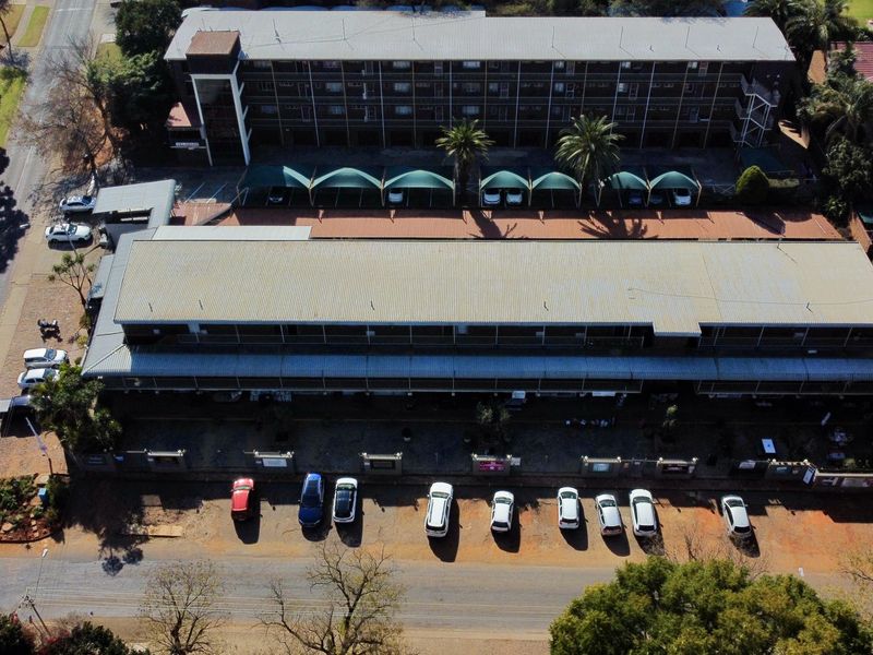 Aerial view of a multi-story apartment complex featuring a corrugated metal roof, dedicated shade cloth carports, and an adjacent paved parking area.