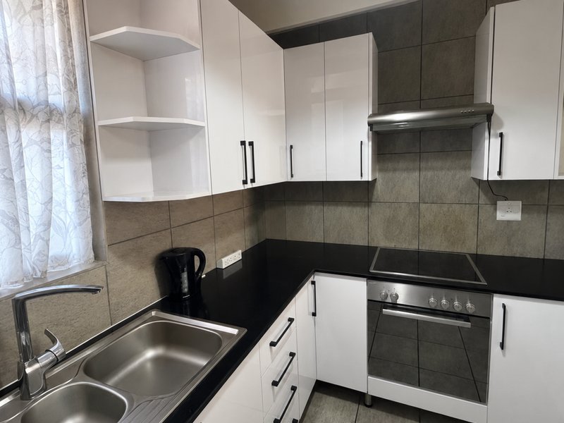 Modern kitchen featuring white high-gloss cabinetry, dark stone countertops, stainless steel appliances, and neutral tiled splashbacks.
