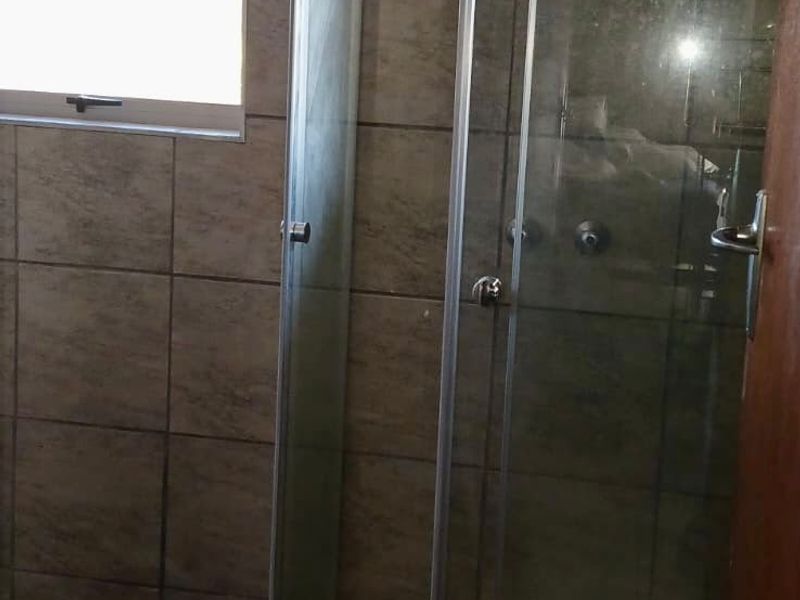 A bathroom featuring a glass shower enclosure with tiled walls and base, currently requiring finishing touches to the base trim and wall area.