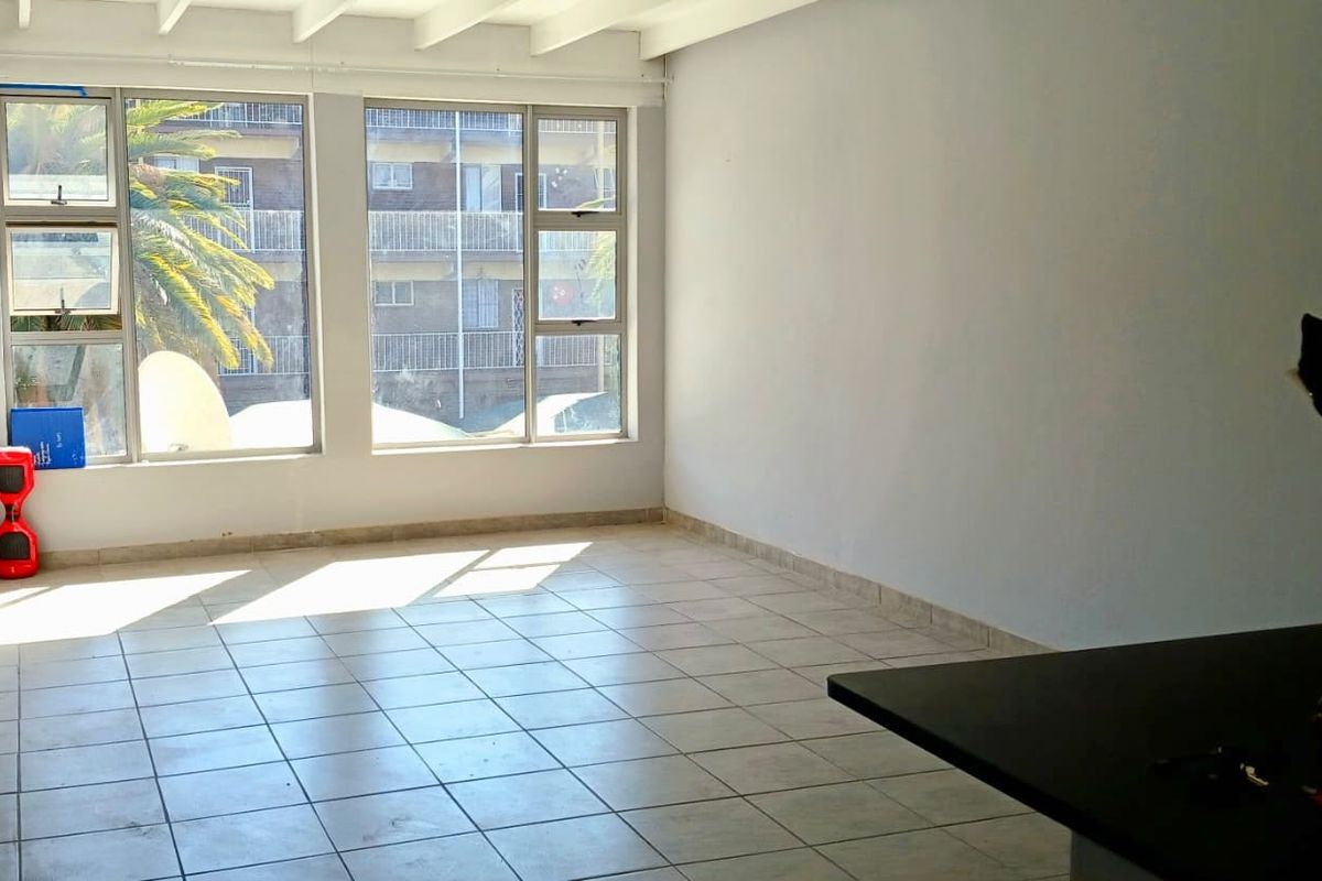 An empty open-plan living area featuring tiled flooring, exposed beam ceilings, and large windows providing natural light.