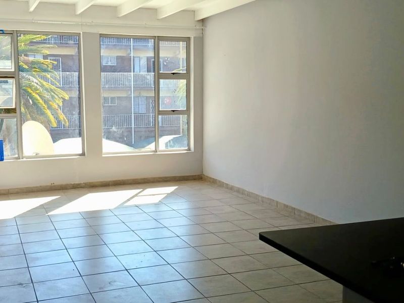 An empty open-plan living area featuring tiled flooring, exposed beam ceilings, and large windows providing natural light.