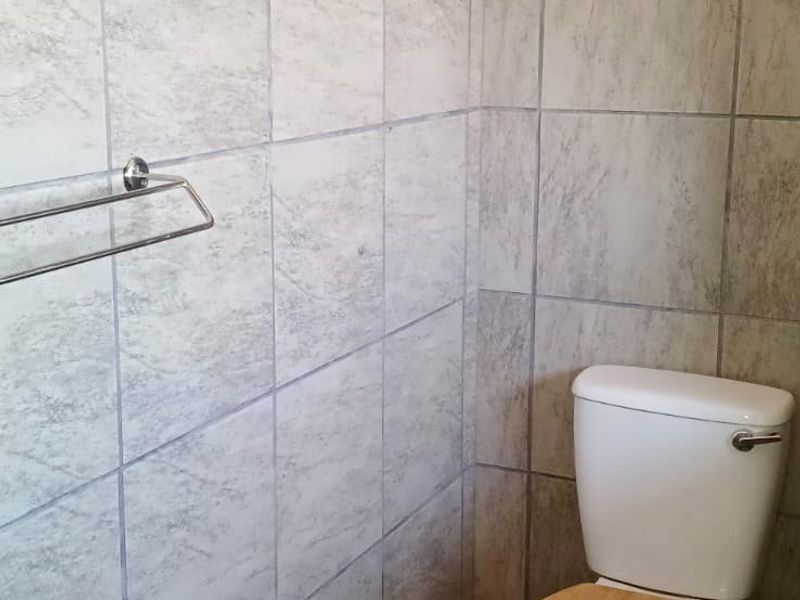 A functional bathroom featuring full-height ceramic wall tiling, floor tiles, a standard toilet, and a wall-mounted towel rail.