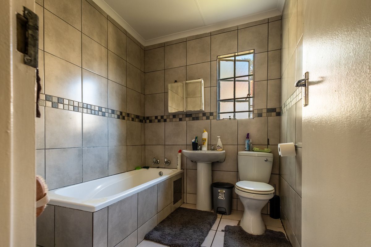 A functional bathroom featuring a bathtub, pedestal basin, and toilet with neutral wall and floor tiling.