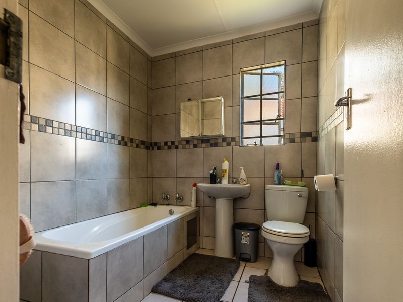 A functional bathroom featuring a bathtub, pedestal basin, and toilet with neutral wall and floor tiling.