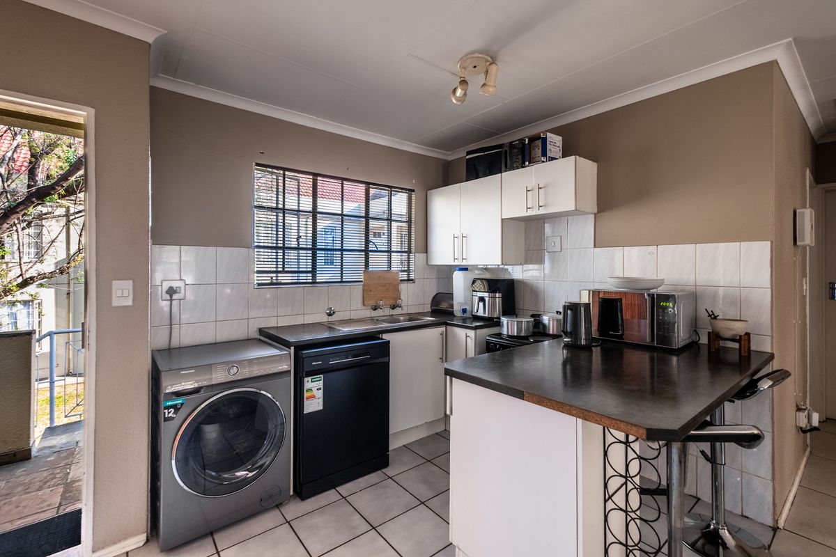 Functional kitchen featuring built-in cabinetry, laminate countertops, tiled backsplash, and tiled flooring, with integrated space for laundry appliances.