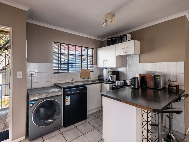 Functional kitchen featuring built-in cabinetry, laminate countertops, tiled backsplash, and tiled flooring, with integrated space for laundry appliances.