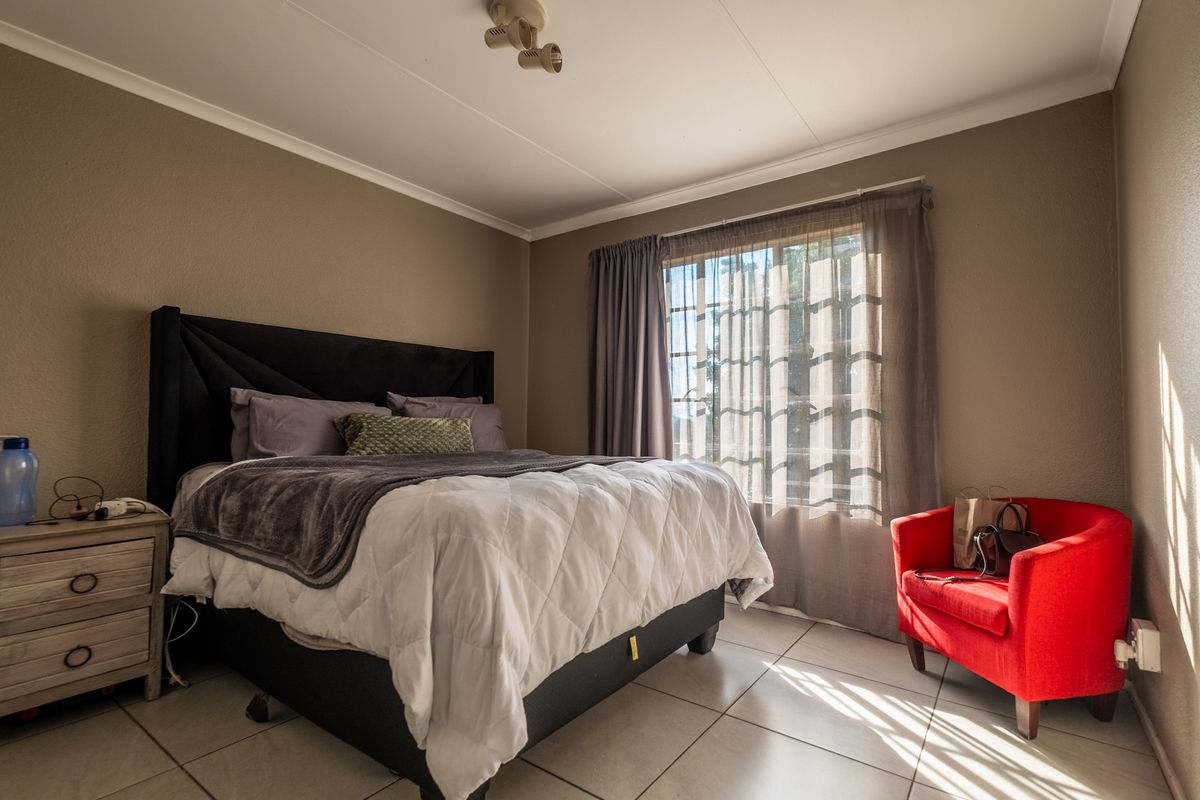 A well-lit bedroom featuring neutral wall tones, tiled flooring, and a ceiling-mounted spotlight fixture, offering a functional and comfortable living space.