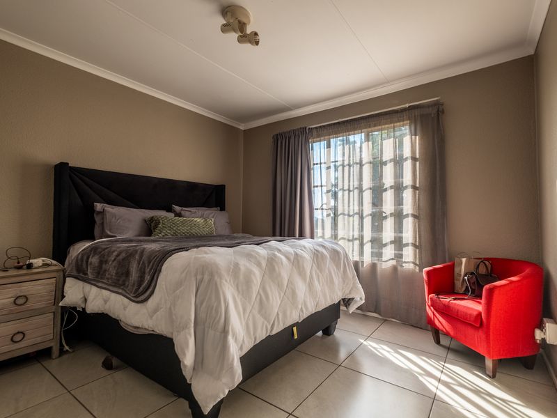 A well-lit bedroom featuring neutral wall tones, tiled flooring, and a ceiling-mounted spotlight fixture, offering a functional and comfortable living space.