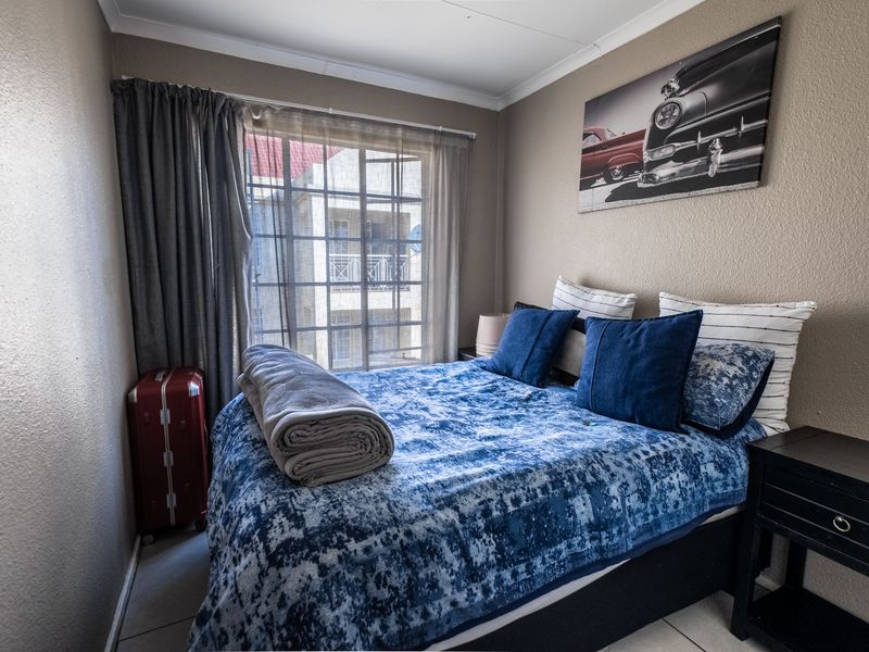 A compact bedroom featuring tiled flooring and a large sliding window, providing natural light and a view of the surrounding apartment complex.