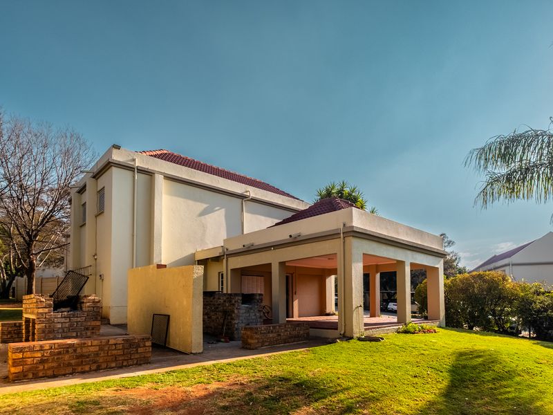 Rear view of the apartment featuring a covered patio area and a built-in brick braai, set within a private garden space.
