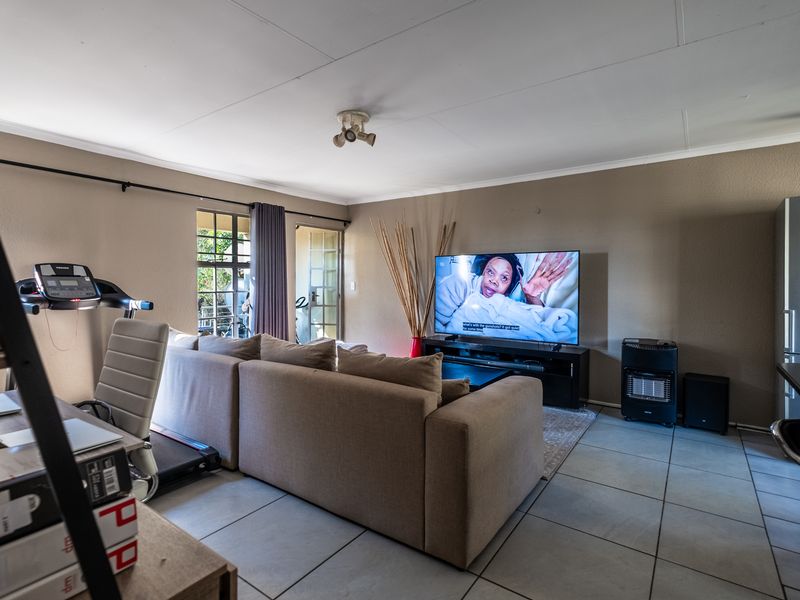 A functional living room featuring tiled flooring, neutral wall tones, and direct access to an outdoor area through a glass-paneled door.
