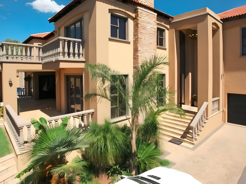 A well-maintained multi-story residential property featuring a paved driveway, covered patio, balcony, and stone-clad architectural details.