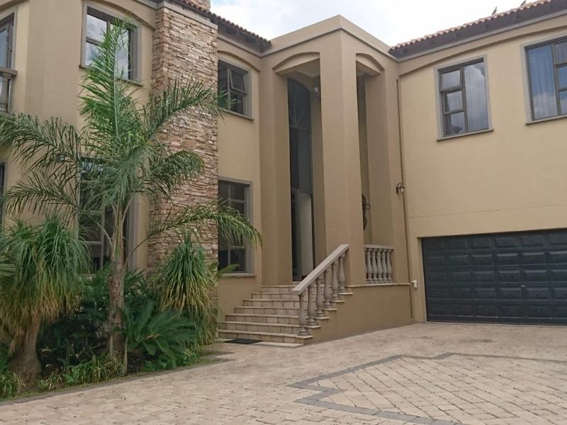 A grand double-story residence featuring stone cladding accents, a paved driveway, a double garage, and an elevated entrance with classic balustrade detailing.