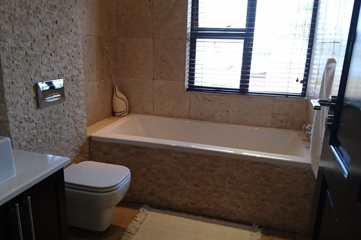 A modern bathroom featuring stone-clad walls, a built-in bathtub, and a wall-mounted toilet with a sleek vanity unit.
