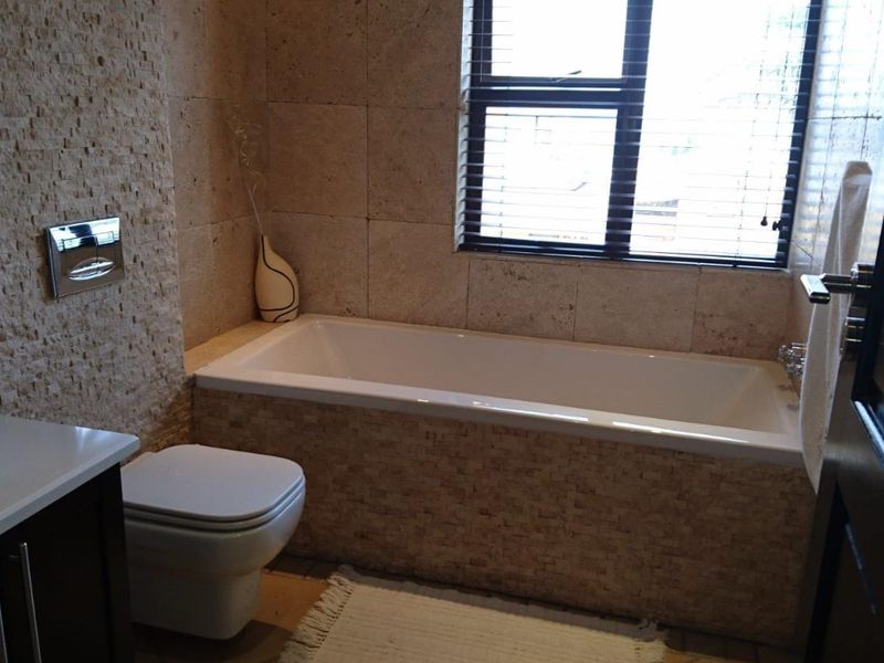 A modern bathroom featuring stone-clad walls, a built-in bathtub, and a wall-mounted toilet with a sleek vanity unit.