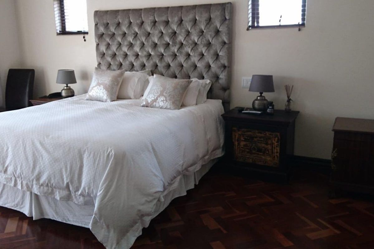 A well-maintained bedroom featuring rich parquet flooring and dual windows with fitted venetian blinds.