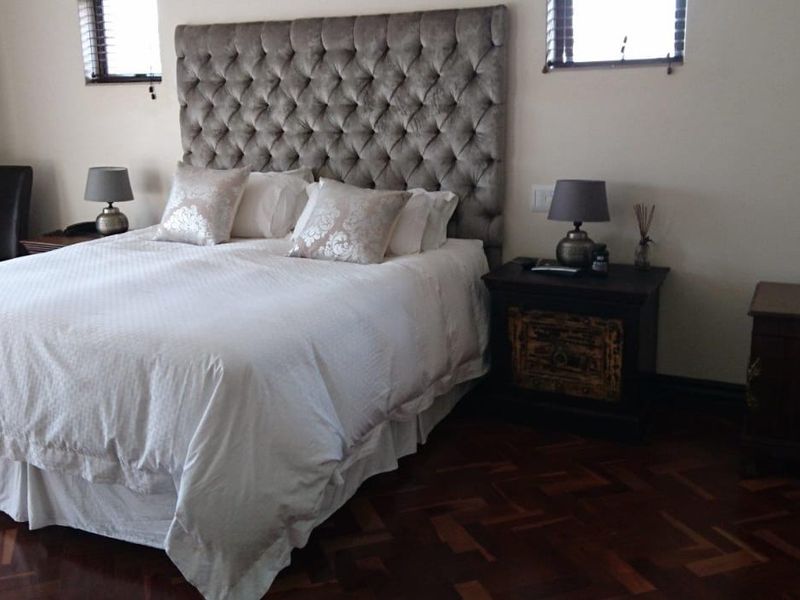 A well-maintained bedroom featuring rich parquet flooring and dual windows with fitted venetian blinds.