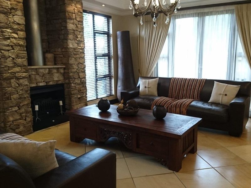Spacious living room featuring a prominent stone-clad fireplace, large windows with natural light, and neutral tiled flooring.