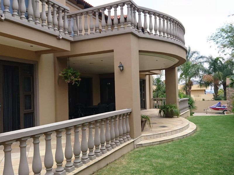 Spacious covered patio featuring stone flooring and a curved balustrade, providing a seamless transition to the rear garden area.