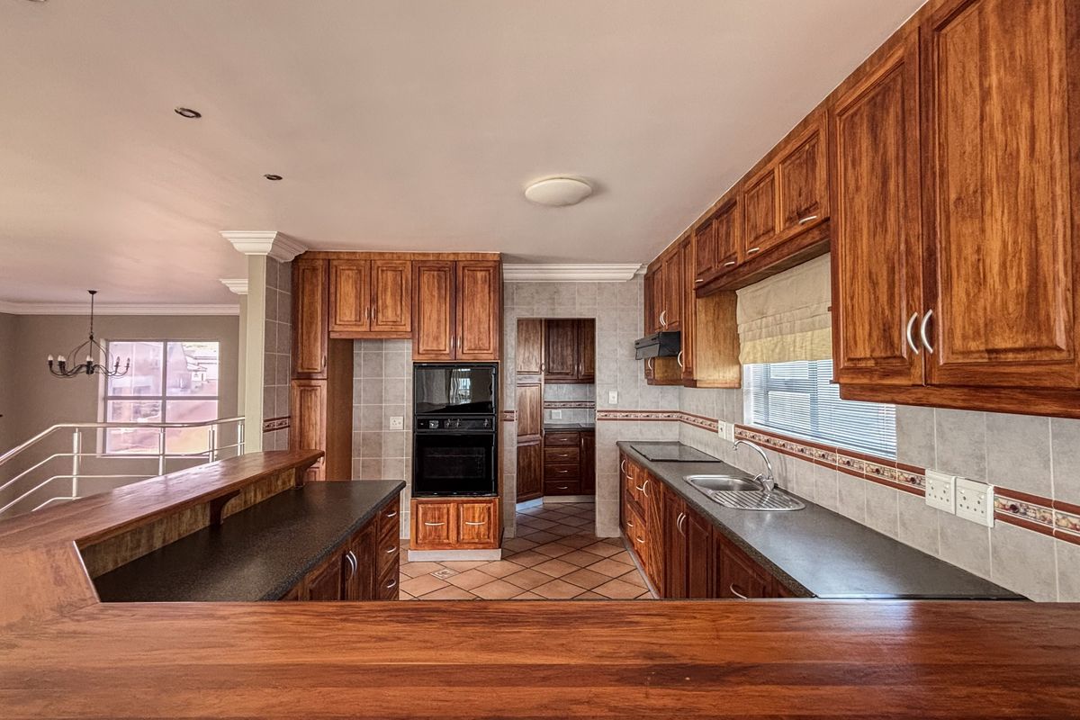 Spacious kitchen featuring extensive wooden cabinetry, built-in oven and microwave, tiled backsplash, and a breakfast bar overlooking the adjacent living area.