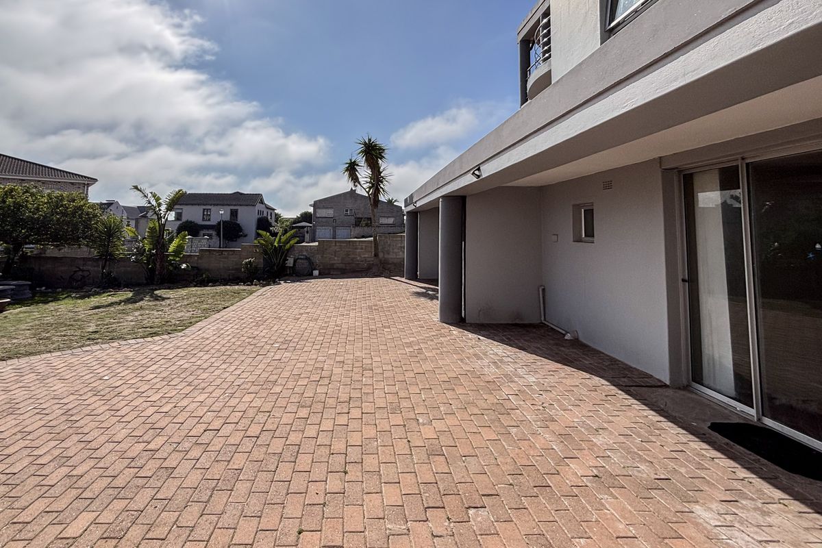 Spacious rear exterior featuring a large brick-paved patio area, covered veranda, and direct access to the home through sliding glass doors.