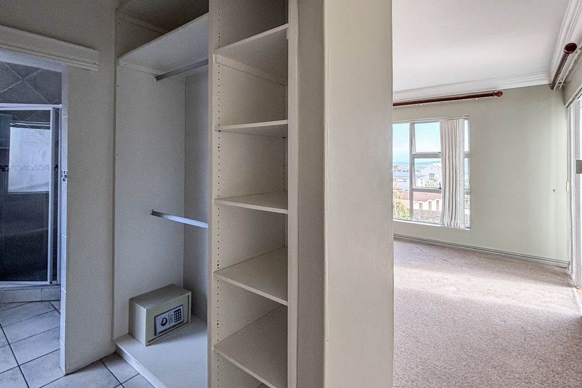 Spacious bedroom featuring built-in wardrobe and shelving, carpeted flooring, and direct access to an en-suite bathroom and outdoor area.