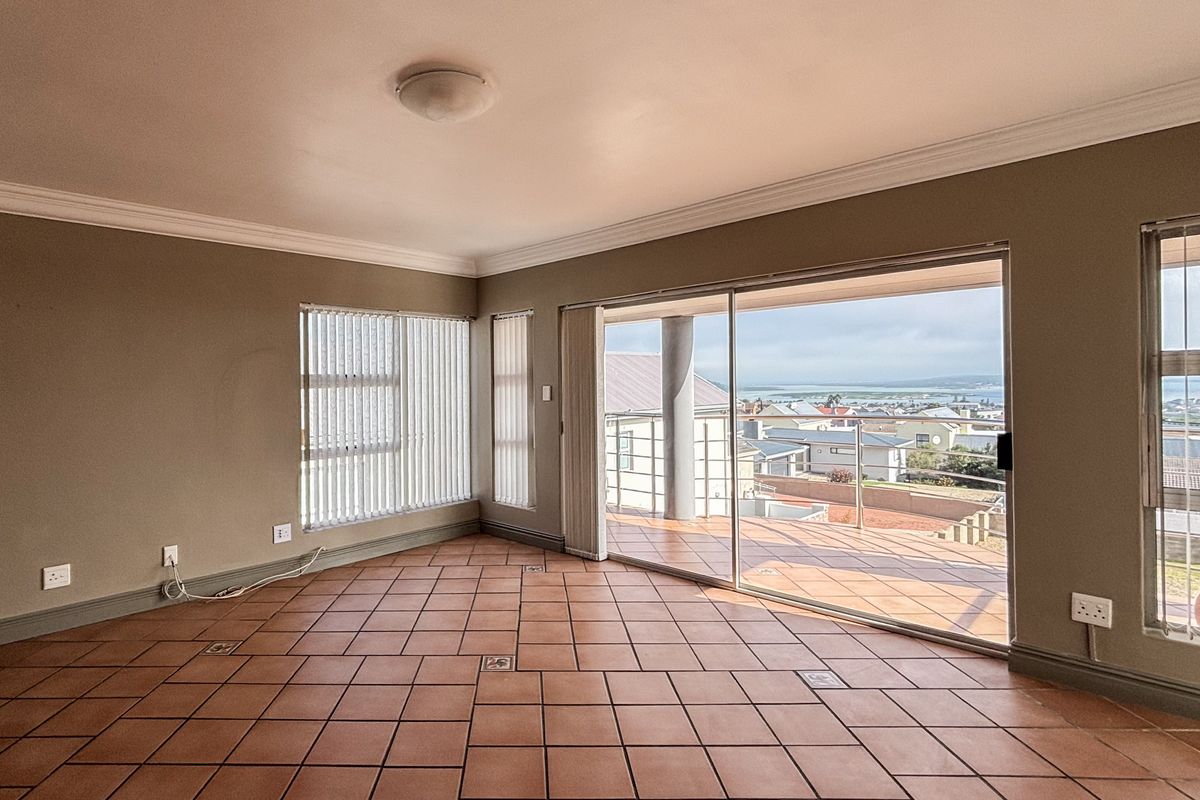 Spacious living area featuring terracotta floor tiles, crown molding, and large sliding glass doors opening onto a balcony with scenic coastal views.