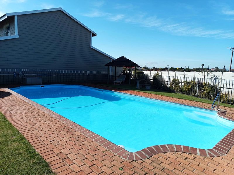 A well-maintained swimming pool area featuring brick paving, a small gazebo, and secure perimeter fencing in a townhouse garden setting.