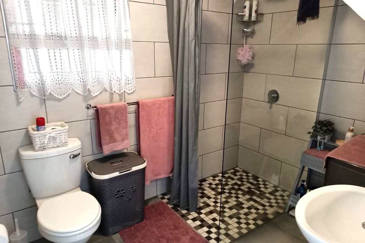 A modern bathroom featuring a walk-in shower with a glass screen, mosaic tiled shower floor, pedestal basin, and neutral ceramic wall tiling.