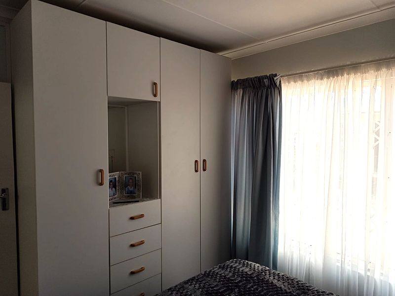 A bedroom featuring white built-in cupboards with integrated shelving and drawers, complemented by a coved ceiling and natural light from the window.